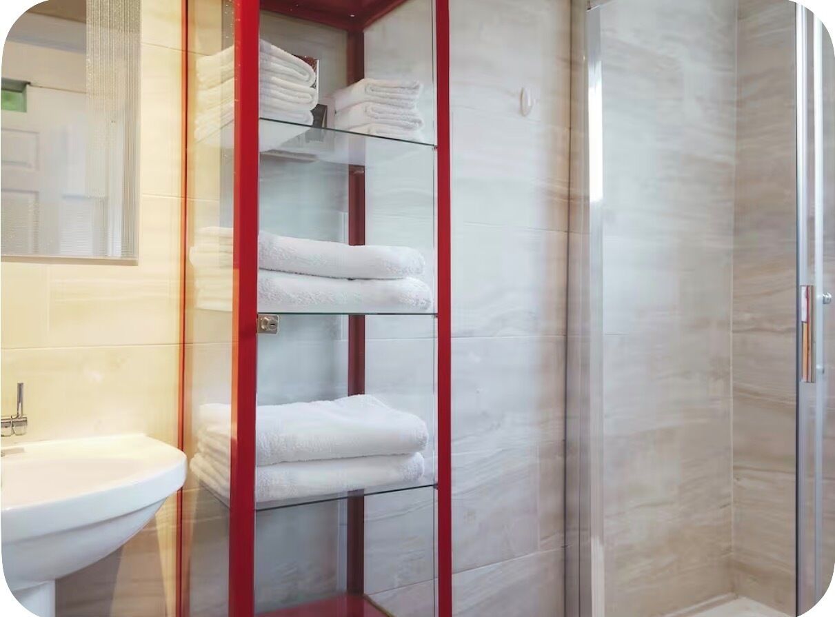 Un baño con cabina de ducha de vidrio, un lavabo y una repisa de vidrio con toallas dobladas.