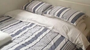 A bed with striped bedding and pillows, a white headboard, and a wooden floor.