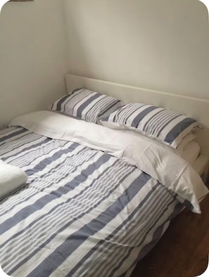 A bed with striped bedding and pillows, a white headboard, and a wooden floor.