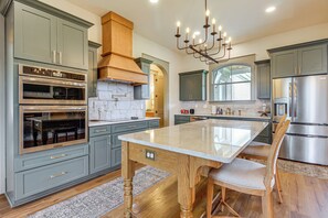 A modern kitchen with built-in appliances, a central island, and a chandelier. - Elevated Designer Home Near Redstone Arsenal (Hazel Green)
