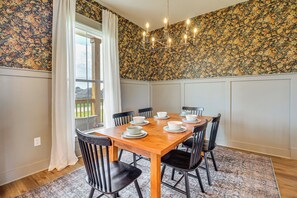 A dining room with a wooden table set for six, surrounded by black chairs, a floral wallpaper, and a chandelier. - Elevated Designer Home Near Redstone Arsenal (Hazel Green)