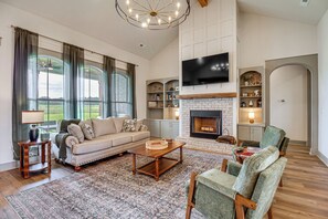 A spacious living room with a fireplace, a large TV, and a sofa. - Elevated Designer Home Near Redstone Arsenal (Hazel Green)