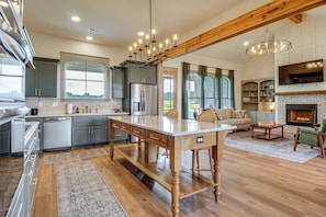 A spacious kitchen with a large island, modern appliances, and a dining area with a fireplace. - Elevated Designer Home Near Redstone Arsenal (Hazel Green)