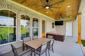 An outdoor patio with a brick wall, a ceiling fan, a TV mounted on the wall, and a dining area with a table and chairs. - Elevated Designer Home Near Redstone Arsenal (Hazel Green)