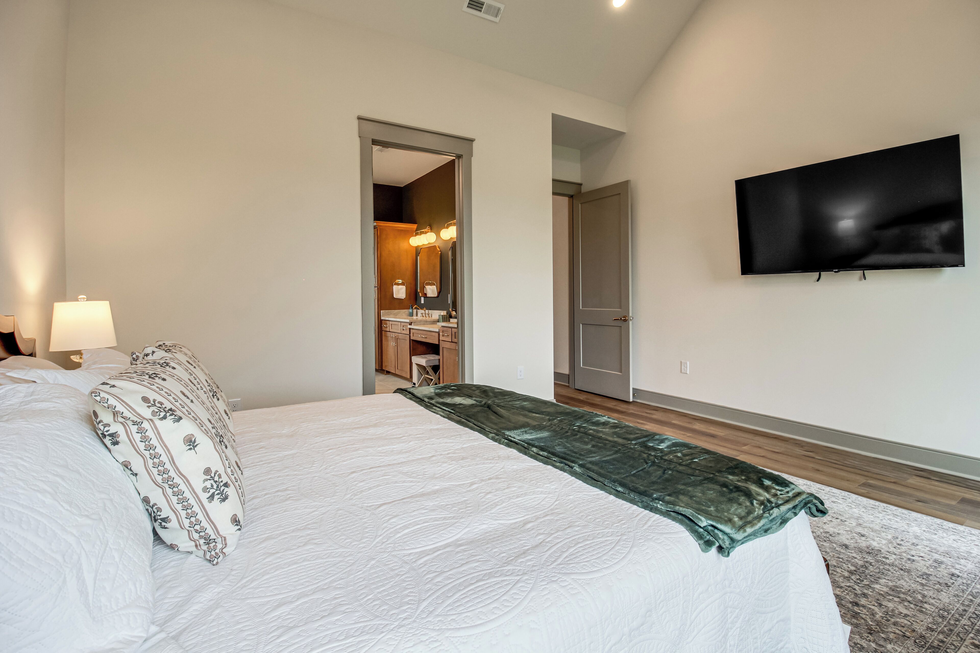 A hotel room with a bed, a TV mounted on the wall, and a bathroom visible through an open door.
