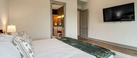 A hotel room with a bed, a TV mounted on the wall, and a bathroom visible through an open door.