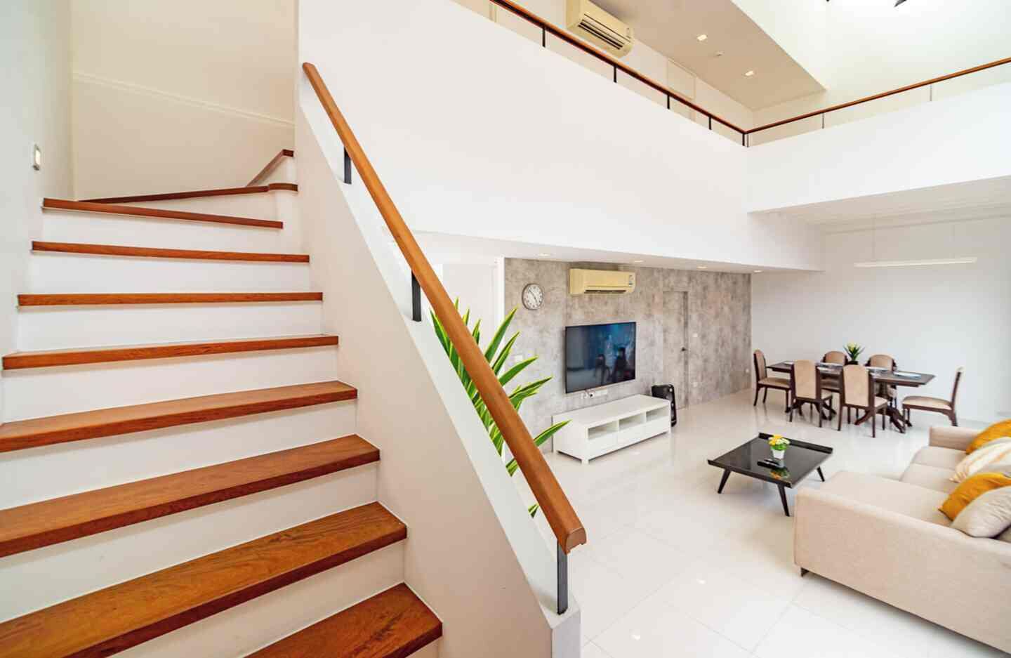 A modern living room with a staircase, a flat-screen TV, a dining area, and a sofa.