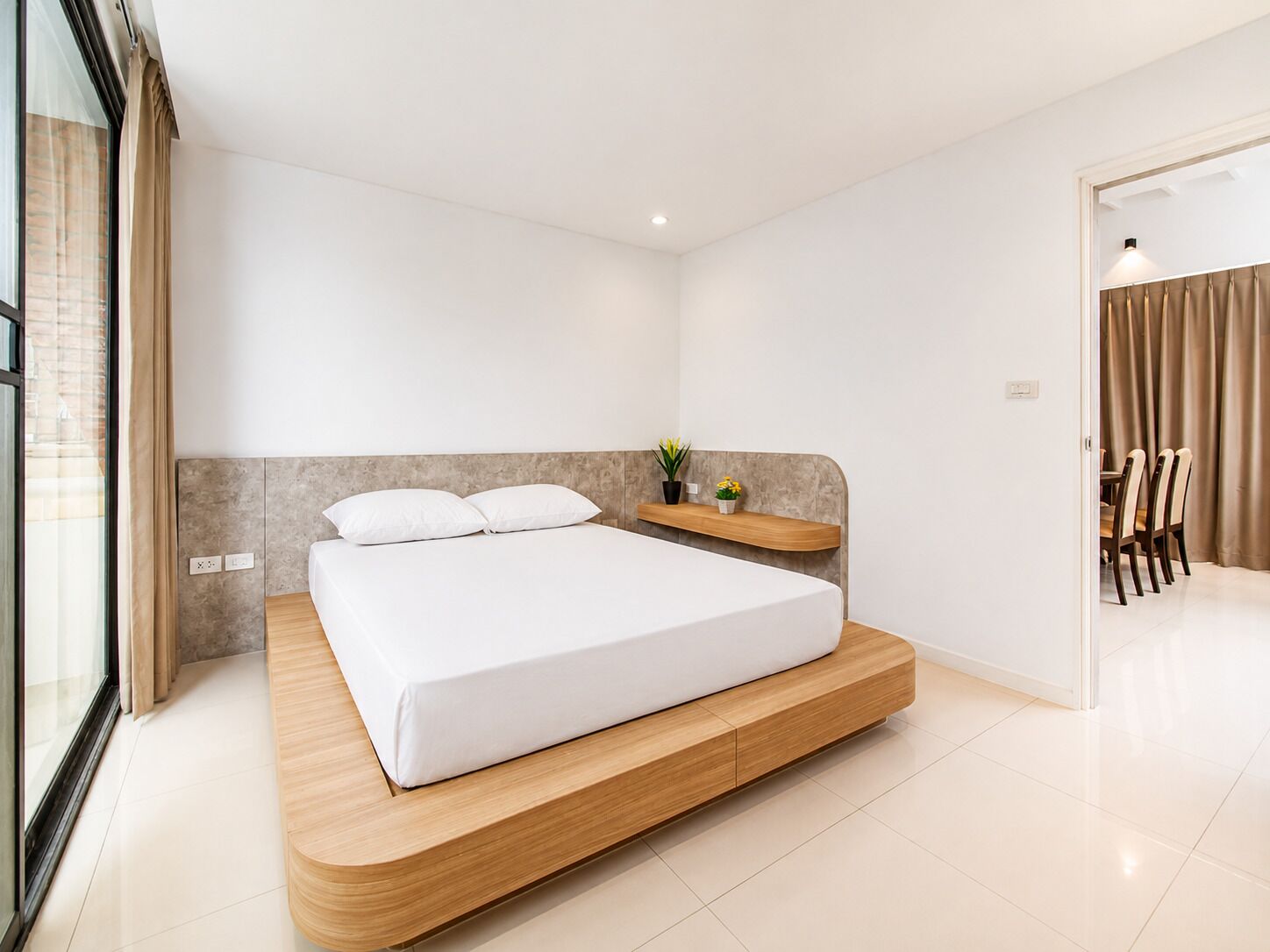 A modern bedroom with a large bed, a wooden bedside table, and a small plant.