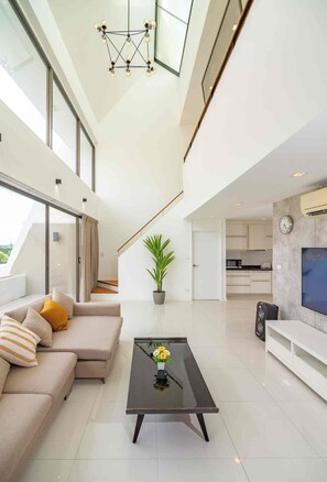 A modern living room with a sofa, a coffee table, and a staircase leading to an upper floor. - Beachfront Duplex in Jomtien 3BR with Pool & Gym. Sea view & Night market. 8ppl (Pattaya City)