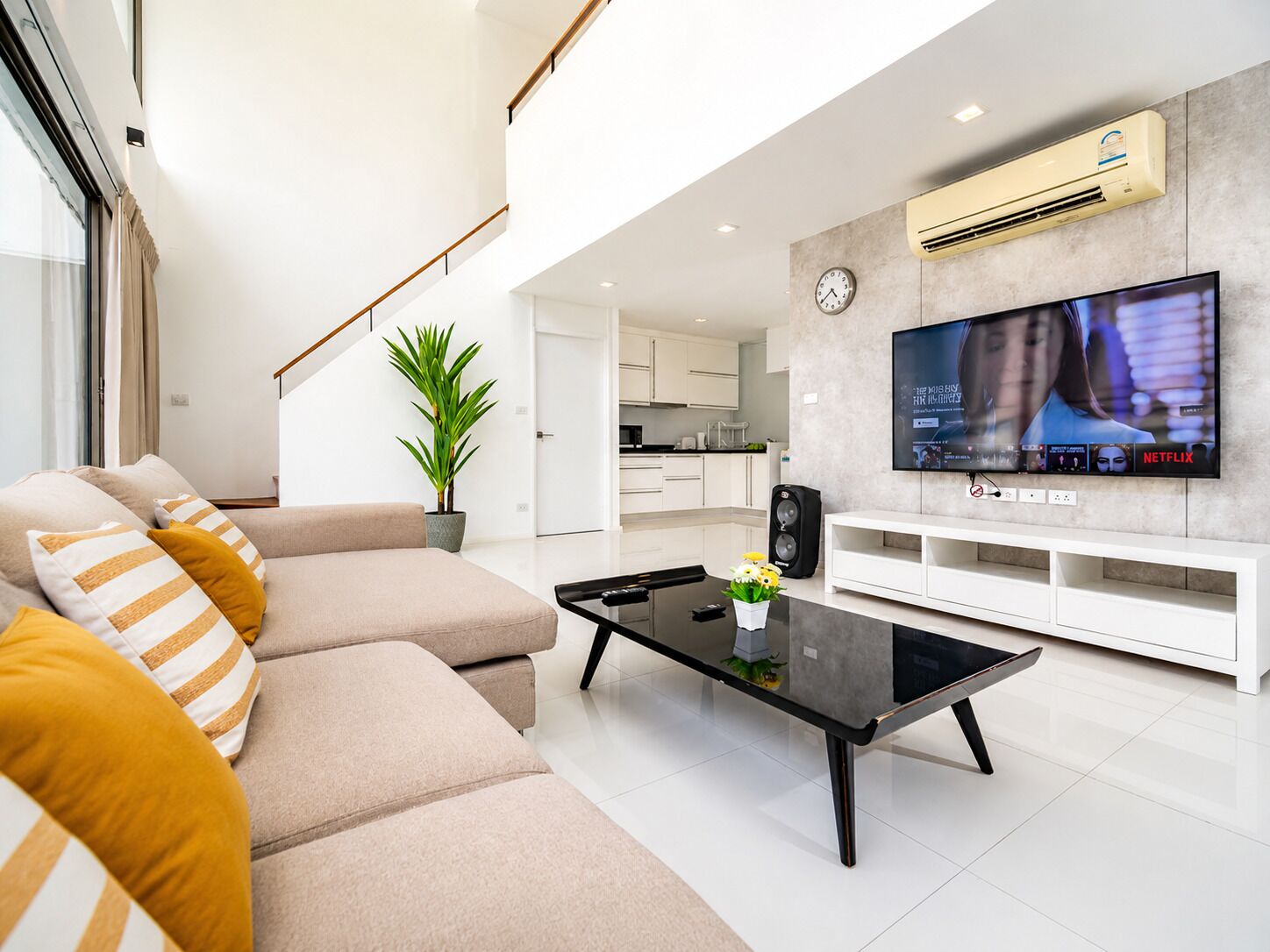 A modern living room with a sofa, a coffee table, a TV, and a kitchen in the background.
