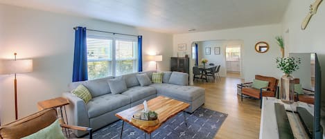 A modern living room with a sectional sofa, a coffee table, and a dining area in the background.