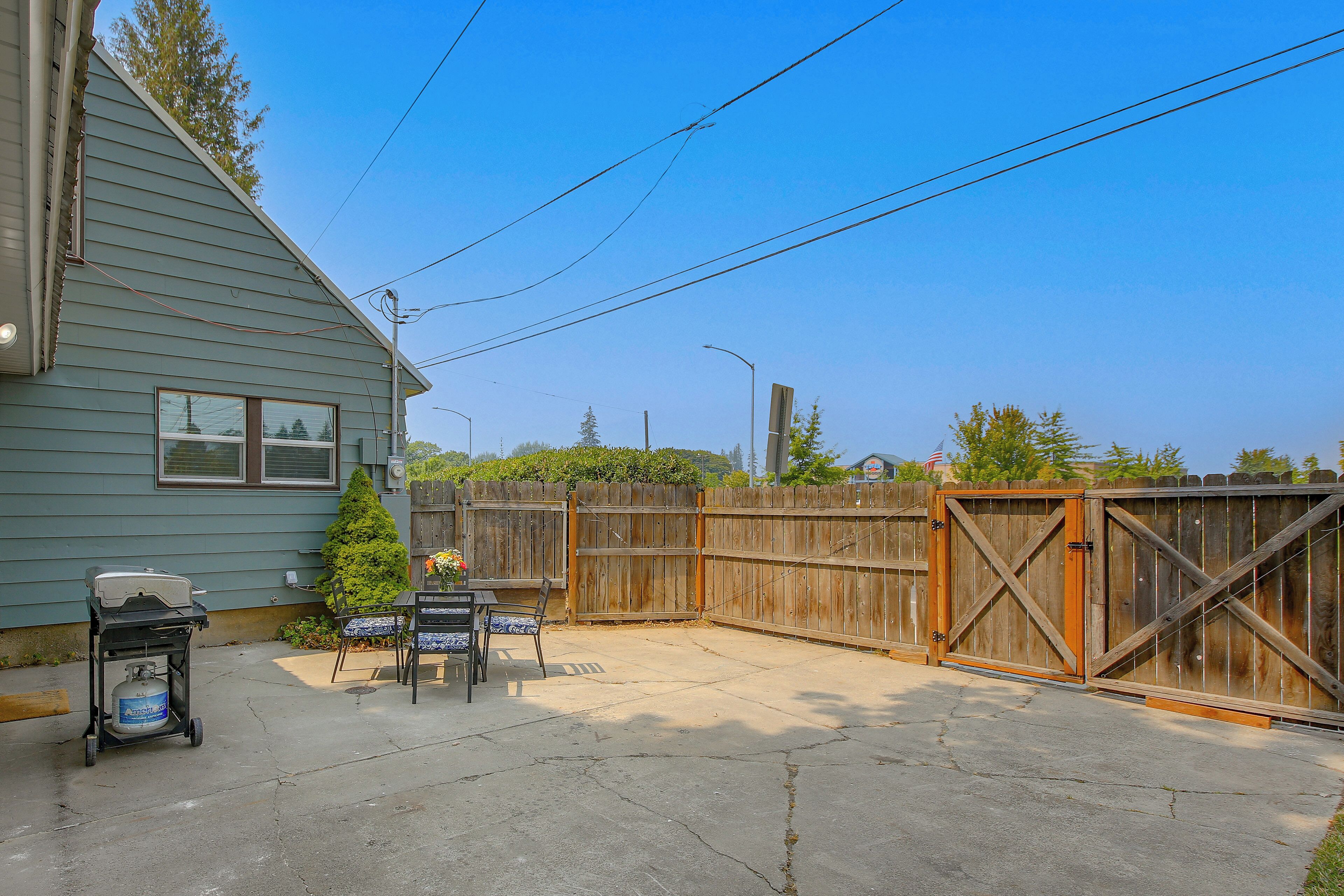A backyard with a patio, a grill, and a wooden fence.