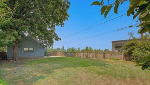 A residential backyard with a house, a wooden fence, and a grassy lawn. - Walk to Dtwn Sandpoint! Family Gem w/ Patio & Yard (Sandpoint)