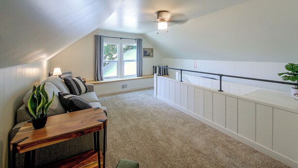 A room with a sloped ceiling, a window with curtains, a radiator, a wooden table with a plant, and a white railing along the wall. - Walk to Dtwn Sandpoint! Family Gem w/ Patio & Yard (Sandpoint)