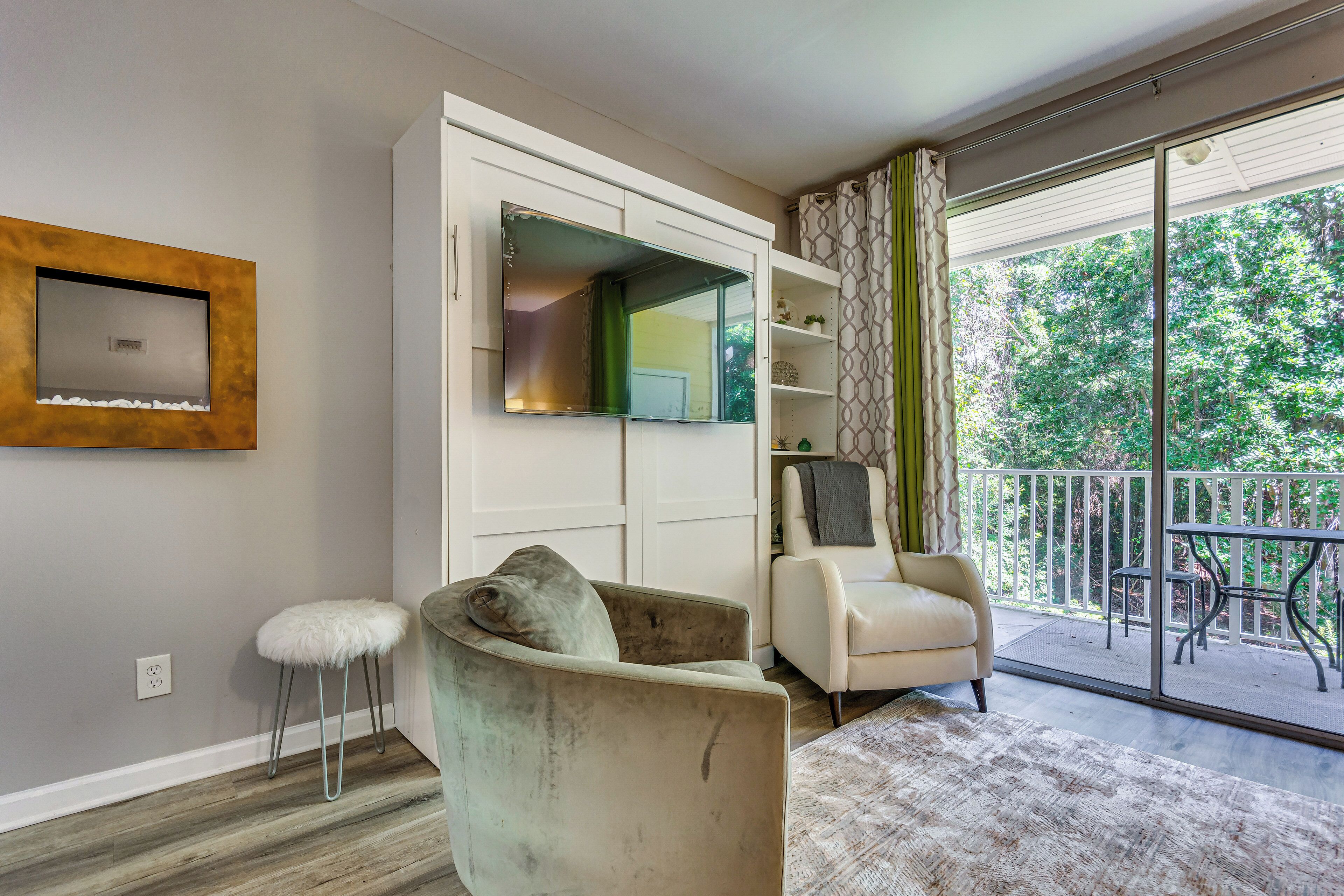 Una sala de estar moderna con un sofá, un sillón, un armario blanco y un ventanal con vistas al verdor.