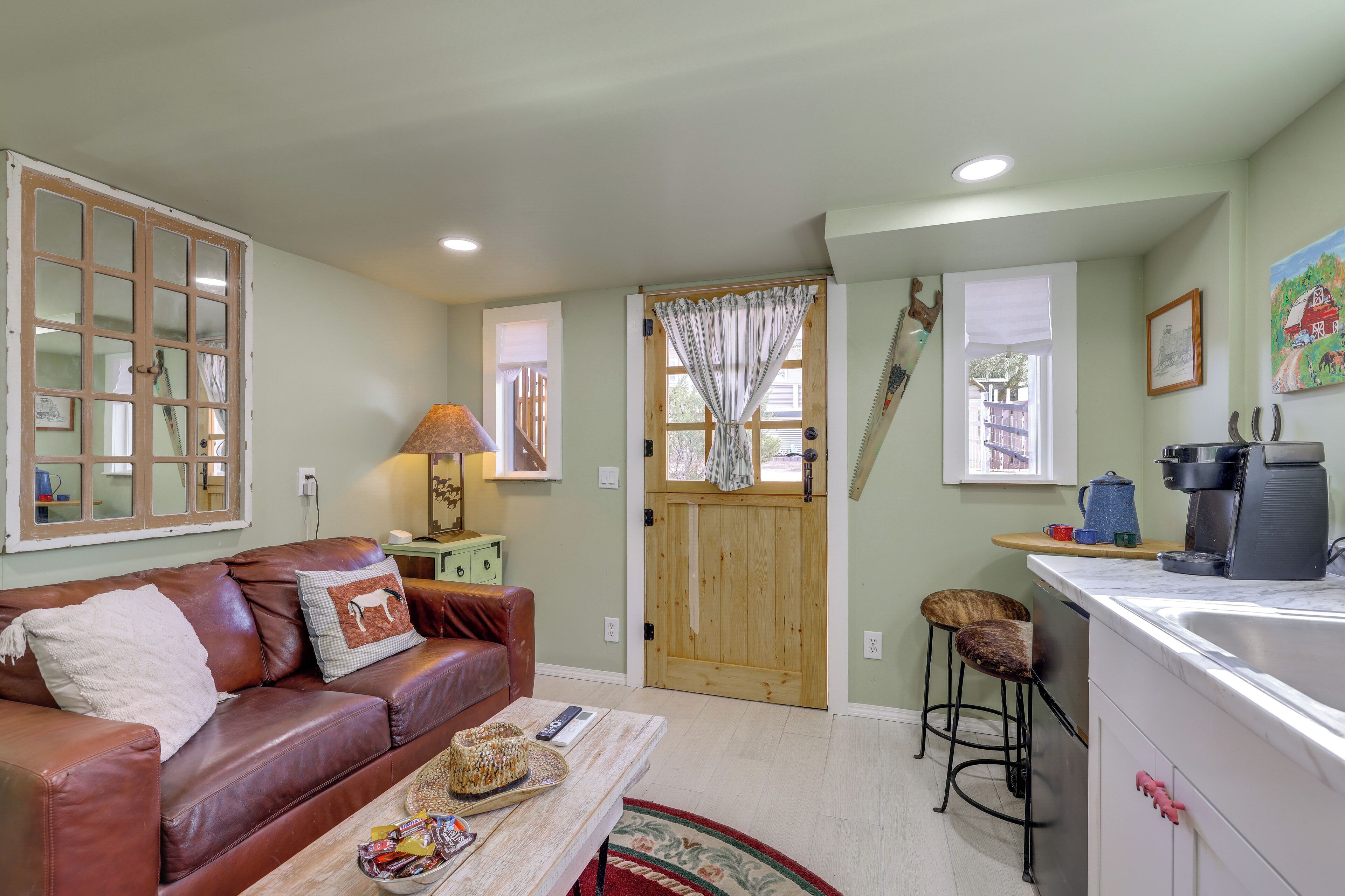 A cozy living room with a leather couch, a coffee machine, and a kitchen area with a sink and bar stools.