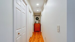 Een hal met witte deuren, een houten vloer, een rode dressoir en een wandlamp.