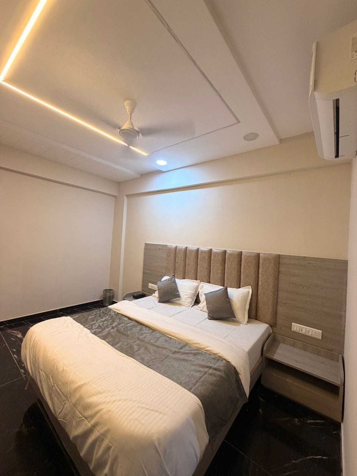 A modern hotel room with a large bed, a ceiling fan, and an air conditioning unit.