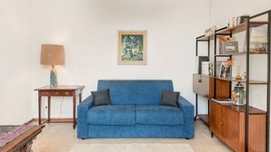 A living room with a blue sofa, a small table with a lamp, a bookshelf, and a framed painting on the wall. - [VillinoAuroraVI] Near the station 5TERRE/Garden (La Spezia)