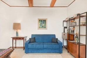 A living room with a blue sofa, a small table with a lamp, a bookshelf, and a framed painting on the wall. - [VillinoAuroraVI] Near the station 5TERRE/Garden (La Spezia)