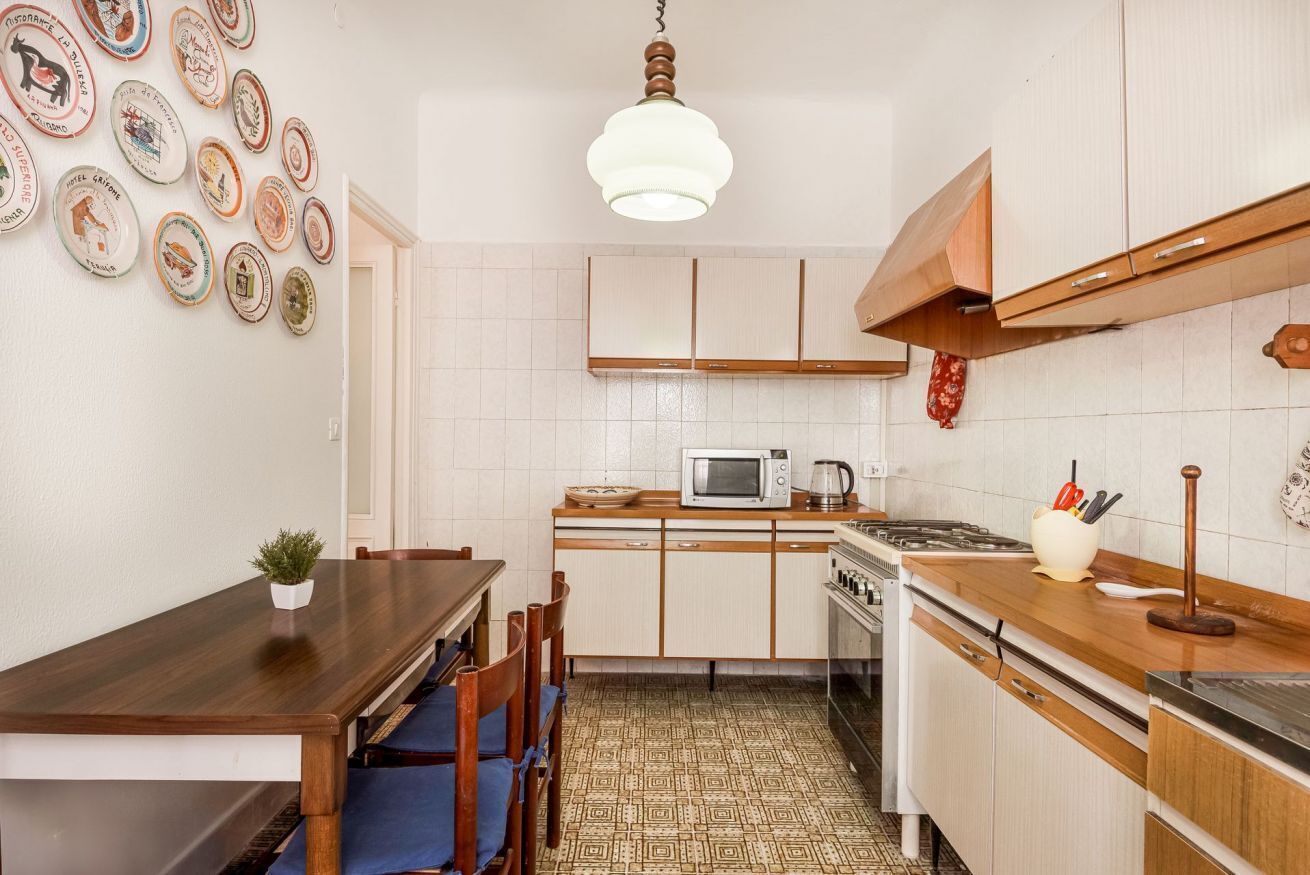 A kitchen with a dining table, chairs, a microwave, stove, cabinets, and a hanging light fixture.