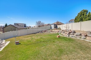 A backyard with a fenced area, a grassy lawn, and a stone wall. - Patio & Mtn Views! Group Getaway in South Jordan (South Jordan)