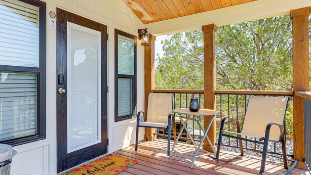 A covered porch with a wooden deck, two chairs, a small table, and a lantern.