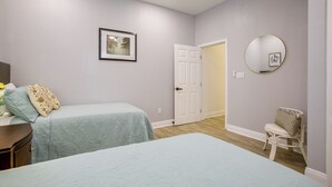 Un dormitorio con dos camas, una mesita de noche, una silla, una puerta y un espejo fijado a la pared.