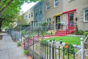 A row of two-story townhouses with a red front door, a small front yard with a stone pathway, and a metal fence. - Charming & Bright Tiny Home: Stadium, River, Metro (Washington)