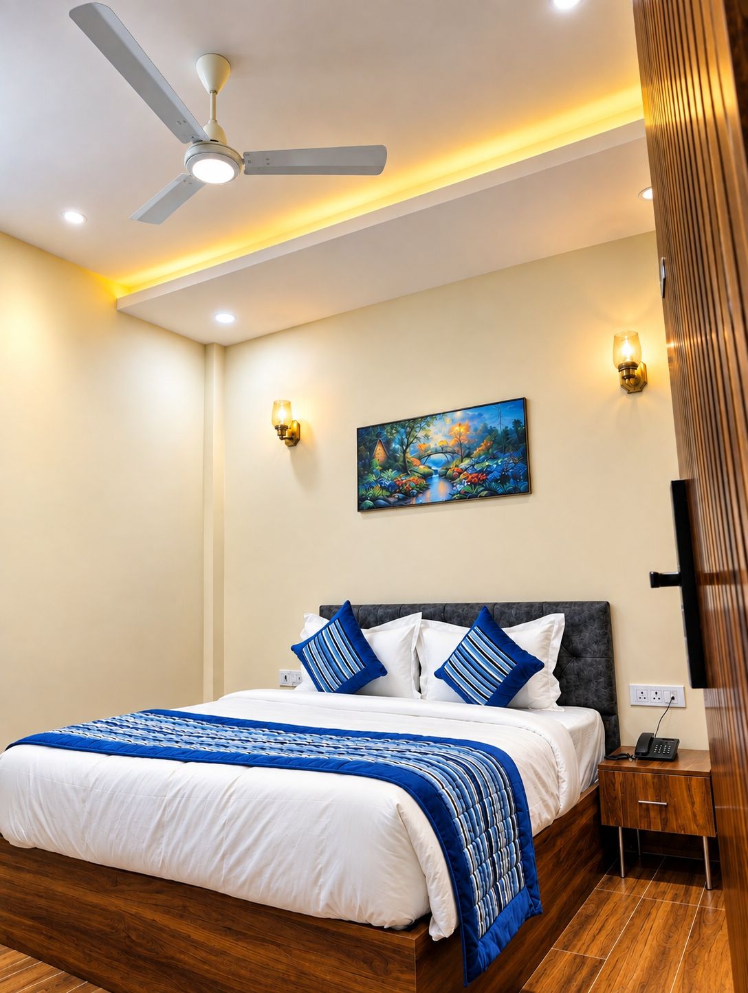 A bedroom with a bed, a ceiling fan, recessed lighting, a painting, and a nightstand with a phone.