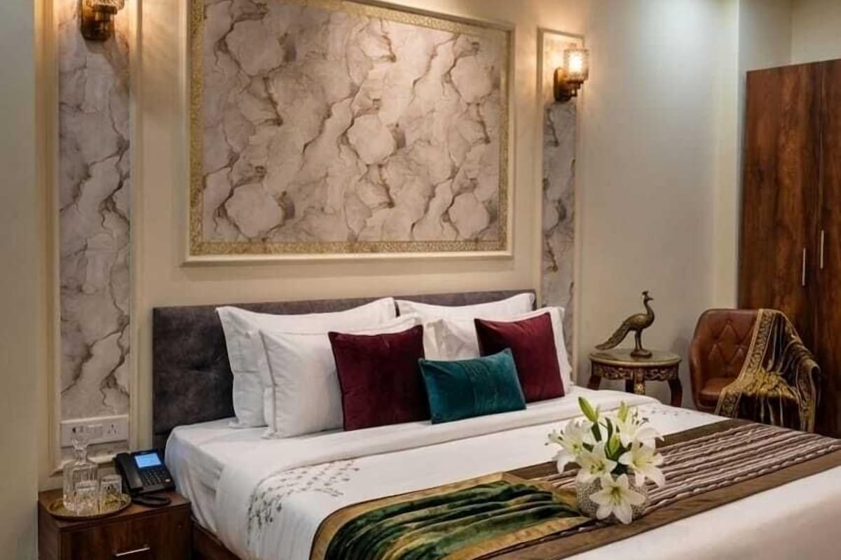 A bedroom with a large bed, a nightstand, a decorative wall piece, and a wooden wardrobe.