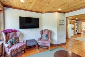 Una habitación con techo de madera, un televisor de pantalla plana en la pared, dos sillones a rayas con cojines, un pequeño reposapiés y suelo de madera.