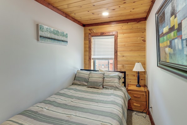 Un dormitorio con cama, mesita de noche, lámpara, ventana con persianas y un cuadro en la pared.
