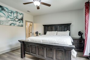 Une chambre à coucher avec un lit en bois foncé, un ventilateur de plafond, un grand tableau abstrait et un rideau rouge à motifs.