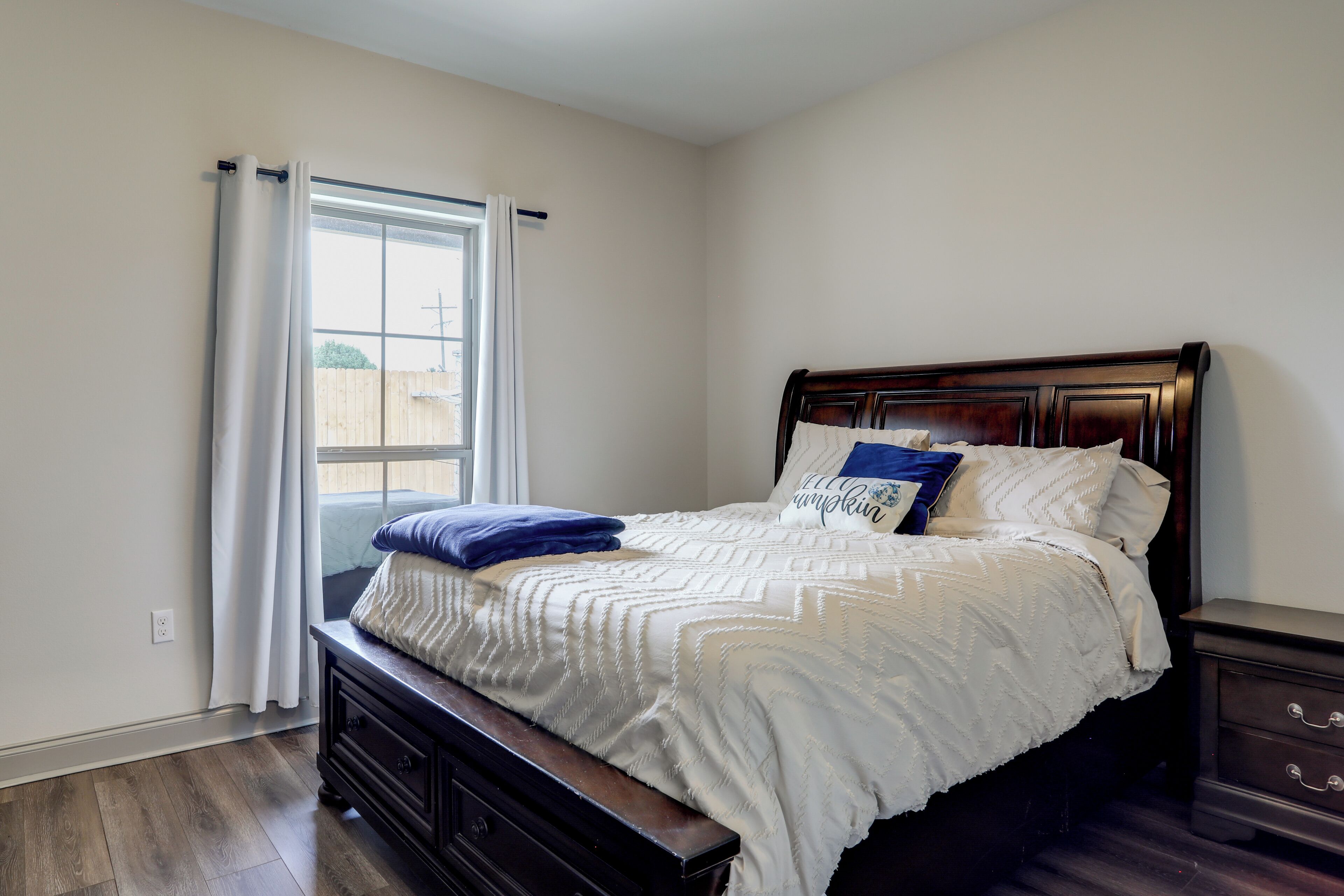 A bedroom with a large bed, a nightstand, a dresser, and a window with curtains.