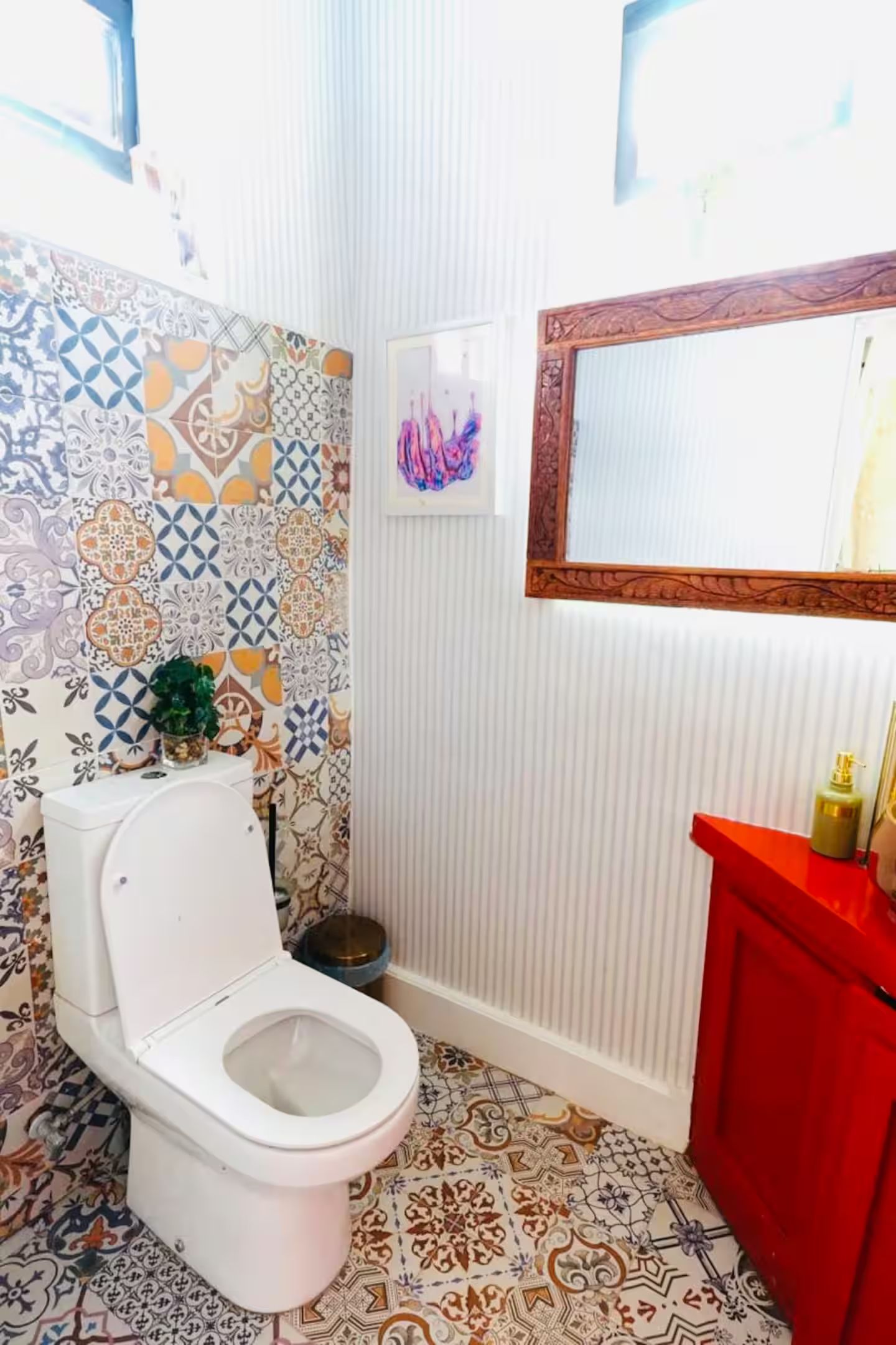 A bathroom with a white toilet, a red sink, and patterned tiles on the walls and floor.