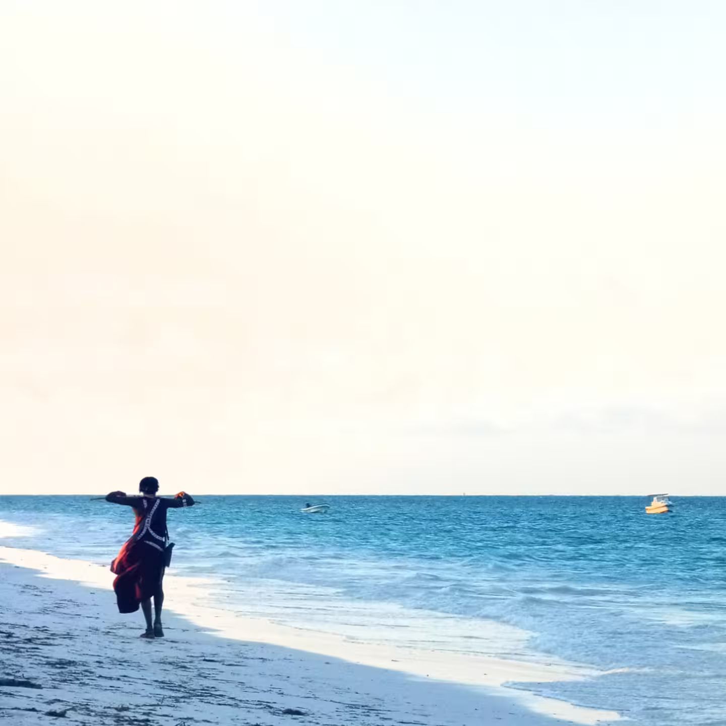 Eine Strandansicht mit einer Person, die auf dem Sand steht und zum Meer blickt.