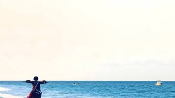 Eine Strandansicht mit einer Person, die auf dem Sand steht und zum Meer blickt.