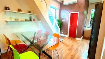 Un espace de salle à manger moderne avec une table en verre et des chaises colorées, une porte rouge et un escalier menant à une autre pièce.