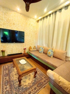 Ein Wohnzimmer mit einer Steinsäule, einem Flachbildfernseher, einem Sofa mit gemusterten Kissen, einem Couchtisch und einem Teppich mit Muster.