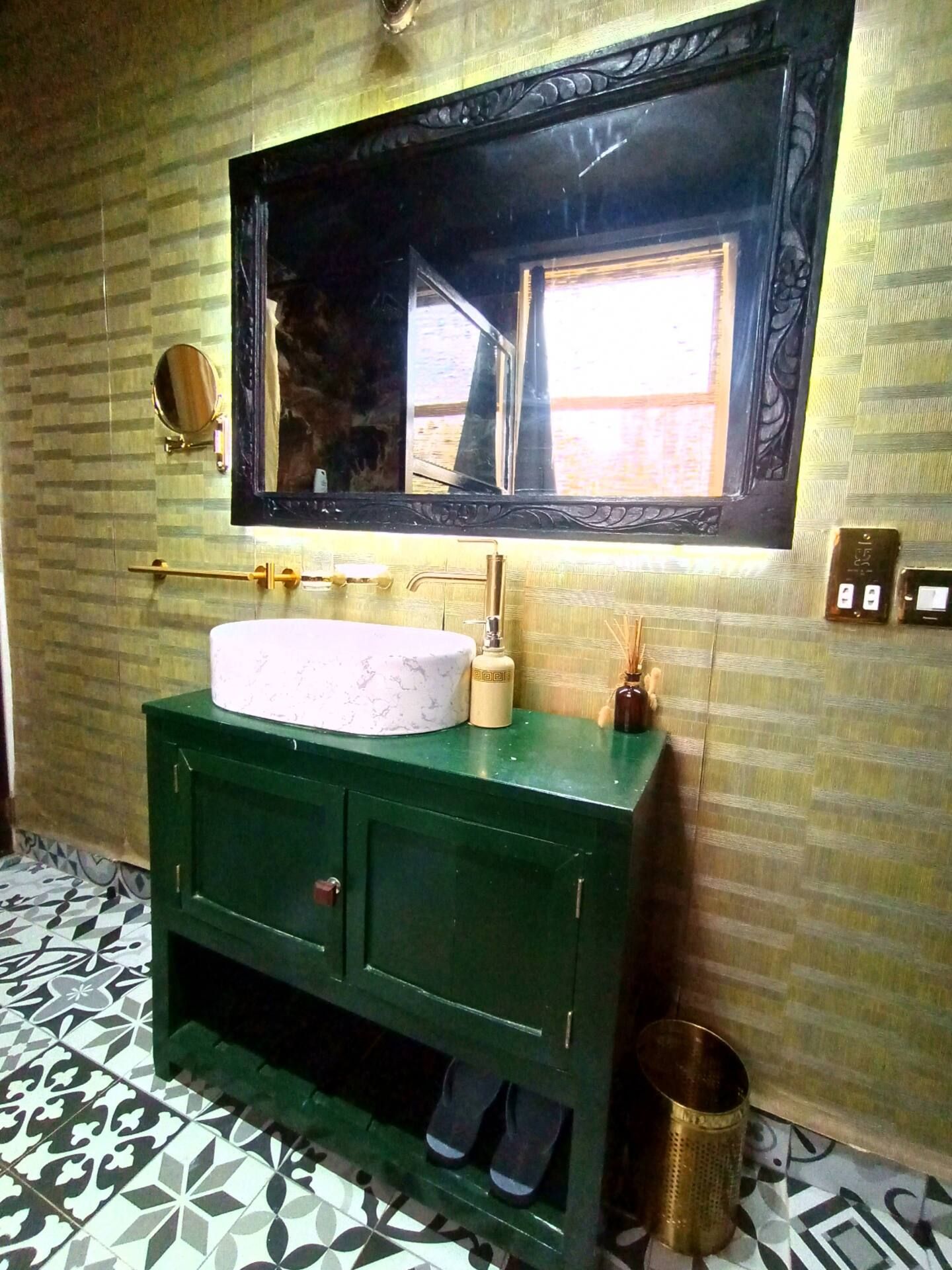 Een badkamer met een groen wastafelmeubel, een ronde spiegel en een witte wasbak.