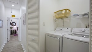 A laundry room with two front-loading washing machines, a yellow laundry basket on a shelf, and a caution sign on the wall. - Stylish Unit 3 Mi to French Quarter & Audubon Park (New Orleans)