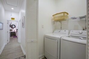 A laundry room with two front-loading washing machines, a yellow laundry basket on a shelf, and a caution sign on the wall. - Stylish Unit 3 Mi to French Quarter & Audubon Park (New Orleans)