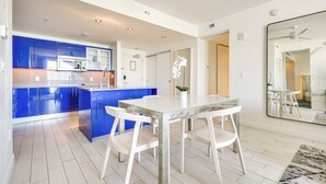Een moderne keuken met blauwe kastjes, een witte eettafel en stoelen.