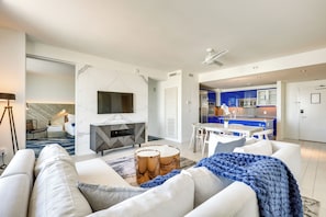 Ein modernes Wohnzimmer mit einer Couch, einem Couchtisch und einem Kamin. Es gibt eine Küchenzeile mit blauen Schränken und einem Esstisch.