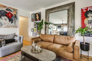 A living room with a brown leather sofa, a grey armchair, a coffee table with decorative items, and a large mirror. - Eclectic Duplex in the Heart of High Point Terrace (Memphis)