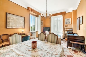 Ein Zimmer mit Esstisch, Stühlen, Fernseher, Bett und einer Kristallleuchter.