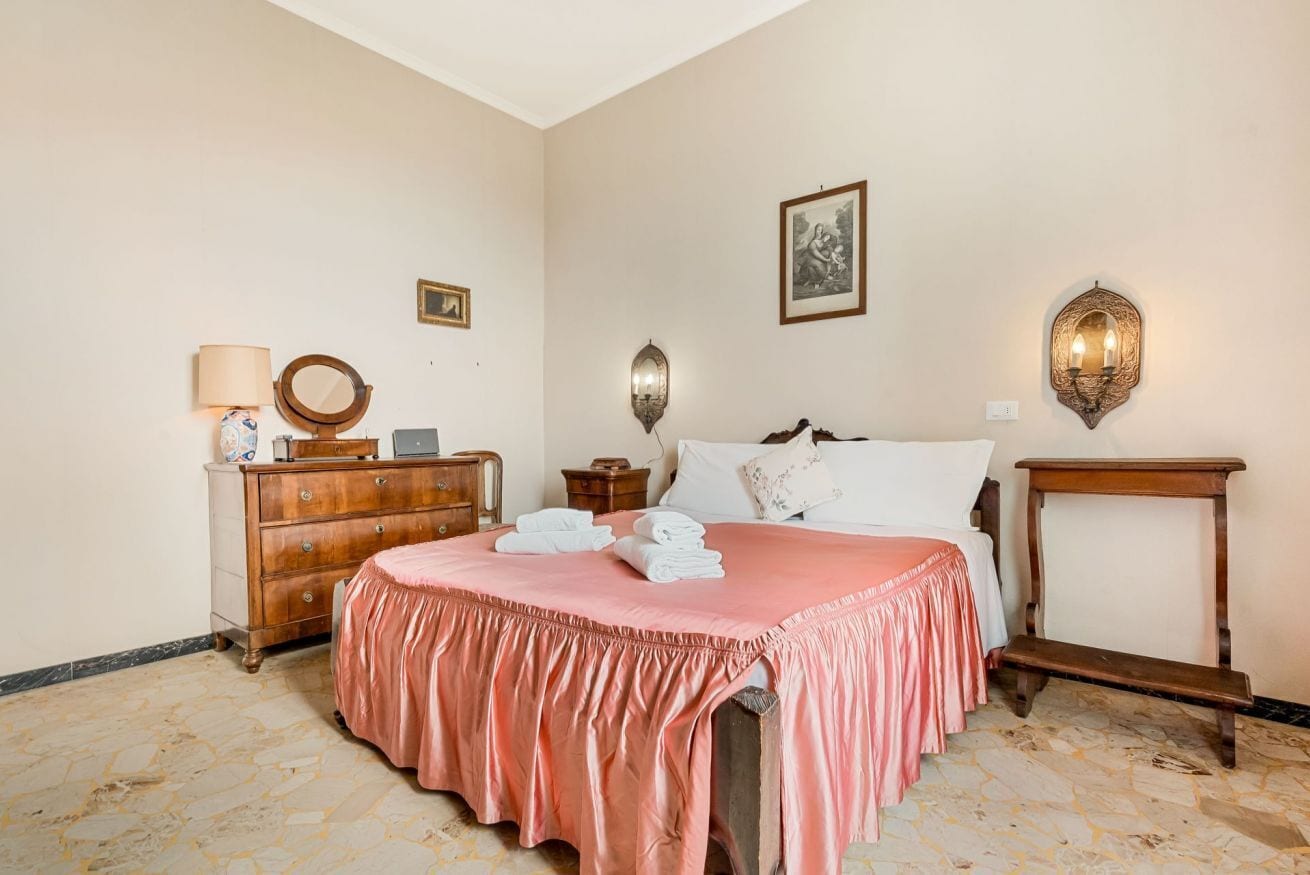 A bedroom with a bed, dresser, bedside table, lamp, and wall sconces.