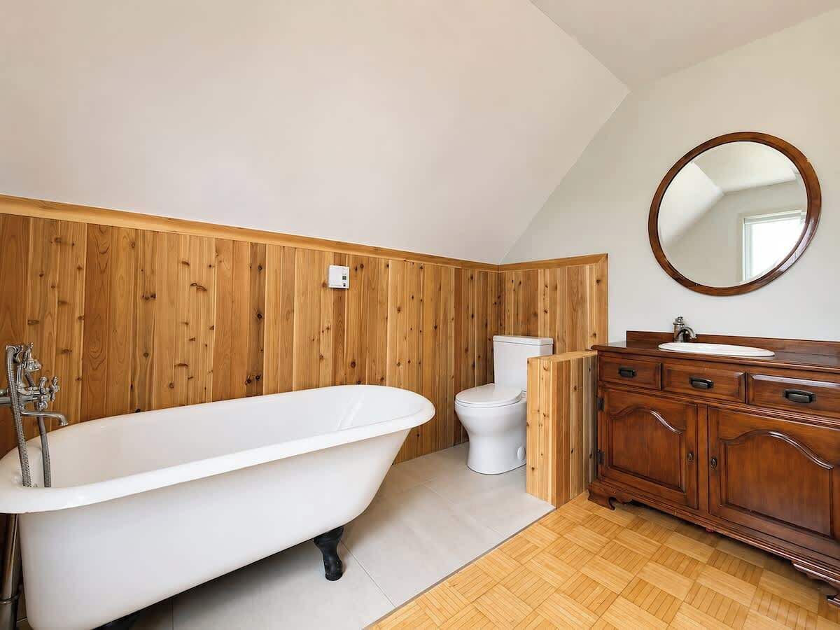 A bathroom with a freestanding bathtub, a toilet, and a wooden vanity with a mirror.