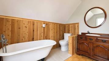 A bathroom with a freestanding bathtub, a toilet, and a wooden vanity with a mirror.